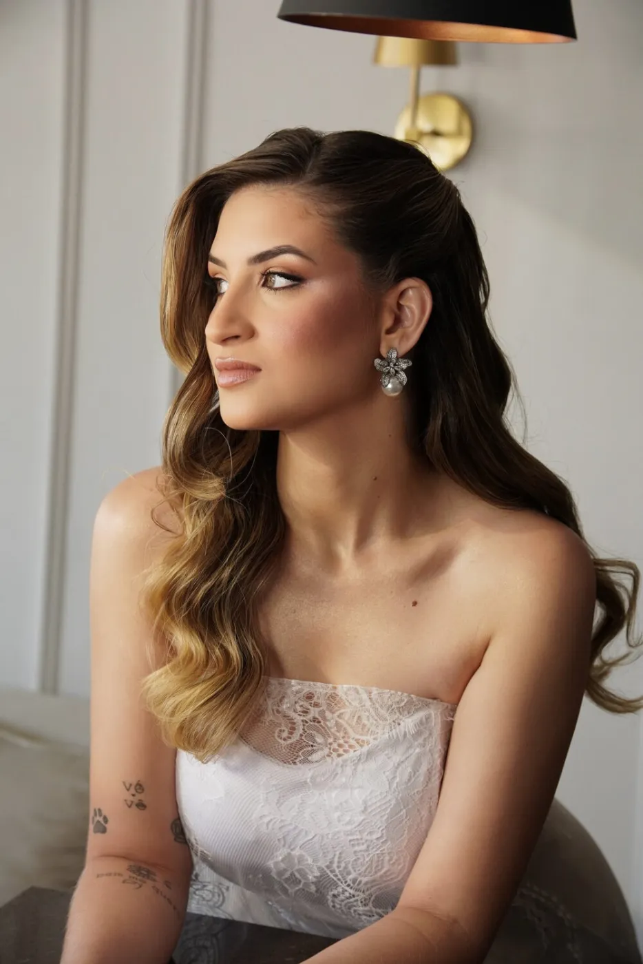 Sentada, olhando para o lado, cabelo ondulado sobre o ombro