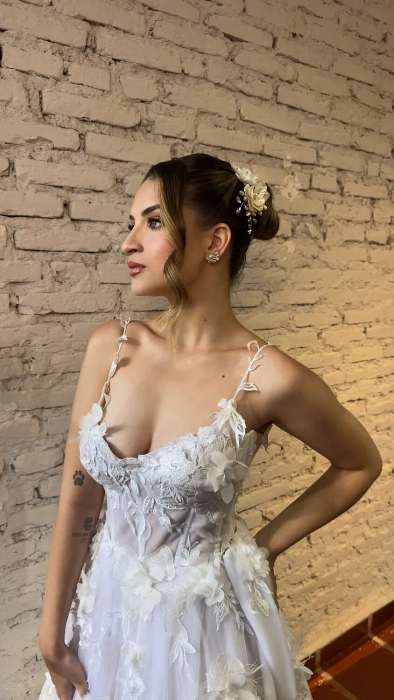 Vestido de noiva bordado, de perfil diante de uma parede de tijolos